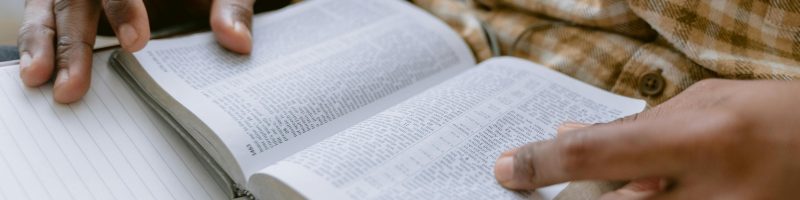 Hands holding an open Bible while taking notes with a pencil.
